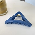 Close-up of a glossy blue triangular hair claw clip with a golden metal spring on a white table - Solid Pale Blue