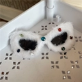 Close-up of white plush cat-eye sunglasses with colorful faux gems on a display shelf - White