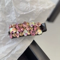 Détail d'une pince à cheveux noire avec strass roses et irisés sur fond de papier froissé - Champagne Rosé