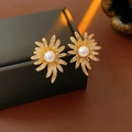 Vista macro degli orecchini a fiore con perla dorata e zirconi su scatola nera - Oro / Oro