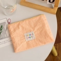 Macro shot of an orange-pink nylon cosmetic bag with a decorative lettered patch and zipper - Orange (Horizontal)