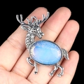 Silver elk brooch with light blue oval gemstone held in hand for size display - Opal (Synthetic)