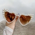 Heart-shaped sunglasses with white pearl trim and brown lenses held against fur background - Glitter Tea Frame Tea Lens