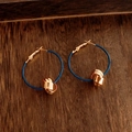 Dettaglio di orecchini a nodo intrecciato placcati oro 18K su sfondo in legno materico - Rame Placcato Oro 18K + Perno Argento 925 / Blu