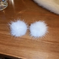 Detalle de dos pendientes redondos de felpa blanca sobre una superficie de madera rústica - Aguja de Plata-Pendientes de Botón de Bola de Pelo Blanco