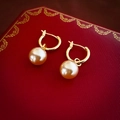 Detalle de pendientes de aro con perlas doradas sobre un joyero rojo decorativo - Clips de Oreja con Perla Champán