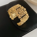 Makroaufnahme einer goldenen Vintage-Manschette mit Hohlmuster auf schwarzem Lederhintergrund - Gold
