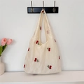 Détail de cerises brodées sur un sac cabas en tulle blanc cassé suspendu à un crochet - Sac Gilet Broderie Cerise