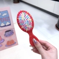Close-up of portable mini hairbrush featuring red handle and colorful wavy bristles - Red