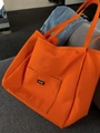 Orange minimalist canvas tote bag with UNSP label and large front pocket on a sofa - Orange