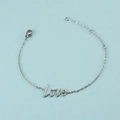 Detalle de una pulsera de cadena de acero inoxidable plateada con dije de letra love - Pulsera de Plata
