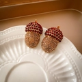 Macro detail of acorn charm with deep red and champagne crystals on ceramic plate - 63# Gold Dark Red Acorn Rhinestone (Silver Earring Post)
