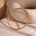 Detail eines gedrehten goldenen Armreifs mit Kugelenden auf Marmoroberfläche - Gedrehtes Seil Offener Stil / Gold
