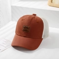 Detail view of a brown mesh truck cap with a square smiley face leather patch and Lucky text - 50cm (1-3 Years) / Orange
