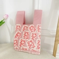 Detail of pink and white knitted tote bag with Becoming Rich slogan on white stool - Pink Becoming Rich Bag