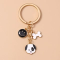 Golden keychain with black smiley face, white bone charm, and spotted dog head pendant - Dog