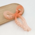 Translucent peach pink bow hair claw clip made of acrylic on a light wood tray - Gradient Jelly Mellow Peach