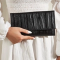 Elegant black pleated evening clutch bag with silk-like sheen held against a white dress - Black