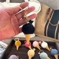Close-up of black ice cream keychain with plush pom pom, golden ring and elegant tassel - Black