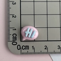 Macro di un ciondolo in resina rosa con scritta HI su un tappetino millimetrato - Fumetto HI-Rosa