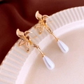 Macro detail of gold flower earrings with drop pearl on a decorative ceramic plate - Silver Needle - Gold Flower Dangle Earrings