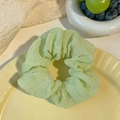 Pale green pleated scrunchie with light airy fabric and bow design on yellow plate - Puff Green