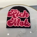 Nahaufnahme einer schwarzen Strickmütze mit rosa Rich Mob Stickerei auf Marmortisch - Kaffee + Rosarot