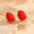 Dettaglio di orecchini ovali dorati con pietre rosse su sfondo di pietra beige - Orecchini a Lobo Rossi (A621)