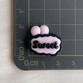 Macro d'un accessoire en résine rose et noir de 2cm avec lettrage Sweet artistique - Base Rose SWEET Noir