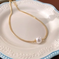 Dettaglio ravvicinato di una collana a catena serpente dorata con ciondolo di perla su piatto - Stile Catena a Serpente Con Perla Singola Placcata in Oro / Oro