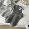 Graue Wollsocken mit hellblauer Strickschleife auf weißem Bettlaken dekoriert - Einheitsgröße / Hellgrau