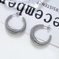 Pendientes en C de plata con textura en espiral sobre un fondo minimalista - Color Acero