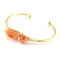 Macro view of gold wire wrapped raw orange crystals on a minimalist open bangle - Red Agate