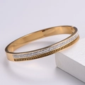 Dettaglio del bracciale rigido dorato 18k con pavé di cristalli e texture intrecciata - Oro