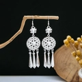 Close-up of ethnic silver feather tassel earrings hanging on a rustic wooden branch - Hollow Snowflake Disc Conical Tassel Style (E4933)