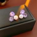Détail de boucles d'oreilles de luxe avec cristaux violets et perles sur boîte noire - Violet
