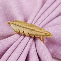 Elegant gold feather alloy napkin ring displayed on a light purple linen napkin cloth - Gold