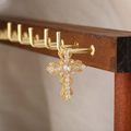 Dettaglio macro del ciondolo a croce dorata con zirconi chiari su collana in acciaio - Stile Croce 19
