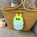 Detail van een kleurrijke rups pluche sleutelhanger met bril op een geweven tas - Groene Kop Blauwe Staart