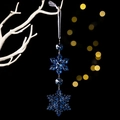 Detail of dark blue acrylic snowflake ornament hanging with ribbon on a black background - Blue