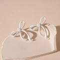 Detailed view of white painted bow-knot stud earrings on a minimalist decorative stone - White Bowknot (Silver Needle)
