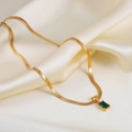 Close-up of a gold snake chain necklace with an emerald zircon pendant on silk - Gold Green Zirconia