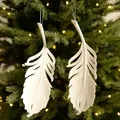 Set of two white glitter feather Christmas ornaments hanging on a warm lit festive tree - Feather Style 2
