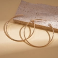 Macro di grandi orecchini a cerchio dorati ritorti geometrici su una pietra beige materica - Stile Liscio / Oro