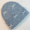 Close-up of light blue knit beanie featuring colorful pastel ribbon bows on soft fabric - Blue Grey