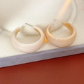 Macro detail of C-shaped resin earrings in beige gradient on a velvet display tray - Off White