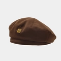 Detail der dunkelbraunen Baskenmütze mit Twill-Stoffstruktur und goldenem Metall-C-Schild - Braun