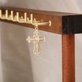 Dettaglio del ciondolo a croce dorata con zirconi su un supporto in legno per gioielli - Stile Croce 17