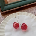 Dettaglio degli orecchini a ciliegia rossi con ganci dorati su un piatto di ceramica - Grande Trasparente Floreale