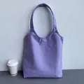 Close-up of a plain purple canvas tote bag leaning against a textured wall with a coffee cup - Purple